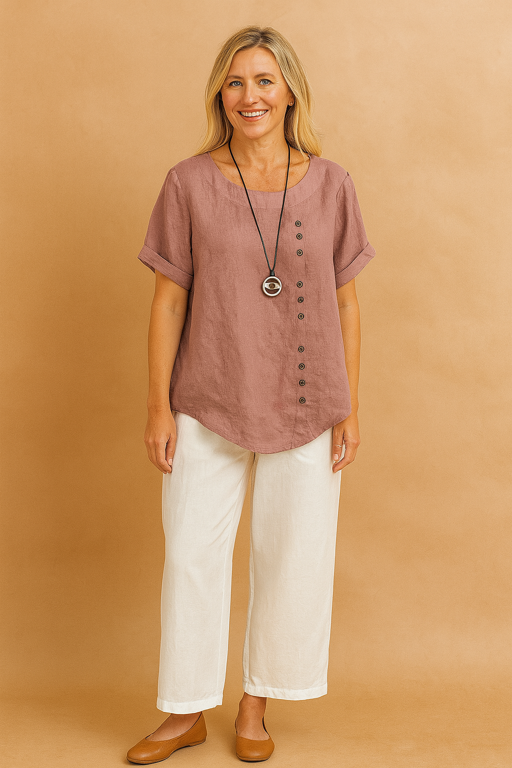 Dusty rose short-sleeve linen blouse with a curved hem, scoop neckline, and asymmetrical row of dark brown buttons, paired with off-white wide-leg pants and a round pendant necklace.