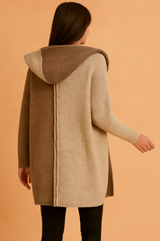 Back view of a two-tone knit hooded cardigan in light beige and medium brown, featuring a vertical seam detail, paired with black leggings.