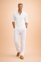 Beige linen long-sleeve Henley shirt with a soft woven texture and three-button placket, paired with crisp white tailored shorts and brown leather slip-on loafers for a refined summer look.