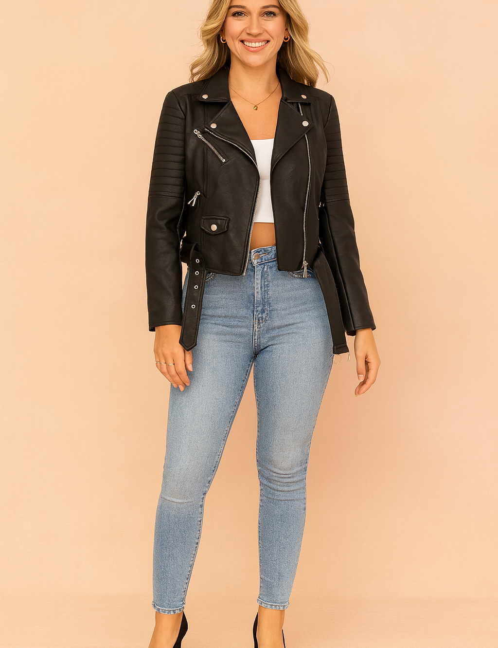 Black biker leather jacket with quilted shoulder panels, belted hem, zip pockets, and silver hardware, paired with light blue skinny jeans, a white cropped top, and black closed-toe heels.