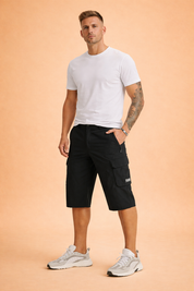 Black utility cargo shorts in smooth matte woven fabric with structured knee-length cut, reinforced seams, zippered side pocket, flap cargo pocket with stitched label, and clean solid color finish, paired with a plain olive-green short-sleeve T-shirt in soft cotton jersey with a minimal, unprinted surface and classic crew neckline, styled with neutral athletic sneakers.