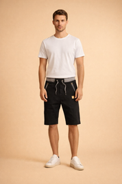Black knee-length cotton men’s shorts with adjustable grey drawstring waistband, structured matte fabric, diagonal zip pockets with metallic detailing, subtle stitched seams, paired with a clean white short-sleeve crew-neck T-shirt in smooth cotton and minimal white low-top sneakers with a matte leather finish.