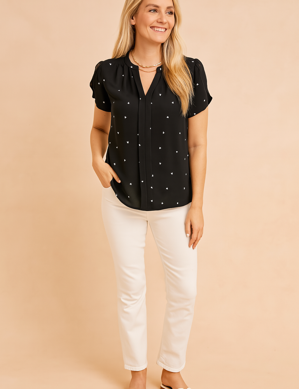 Short-sleeve black blouse with tiny white heart prints, pleated front detailing, and relaxed hem, paired with slim white trousers and white sandals.