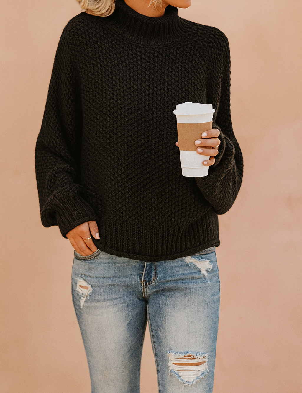 Black chunky knit turtleneck sweater paired with light blue distressed jeans, styled casually with a takeaway coffee cup.