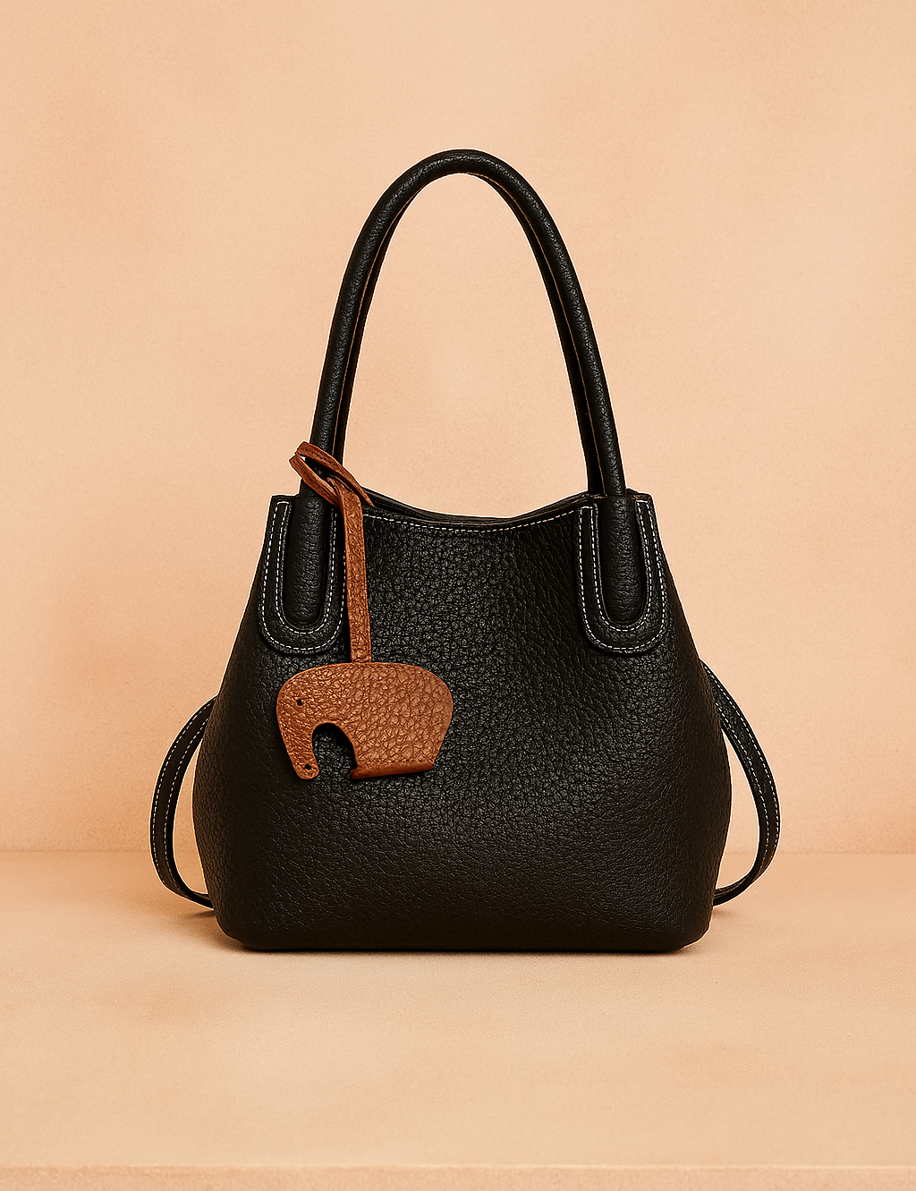 Black pebbled leather tote bag with white stitching, double handles, and a brown elephant-shaped charm.