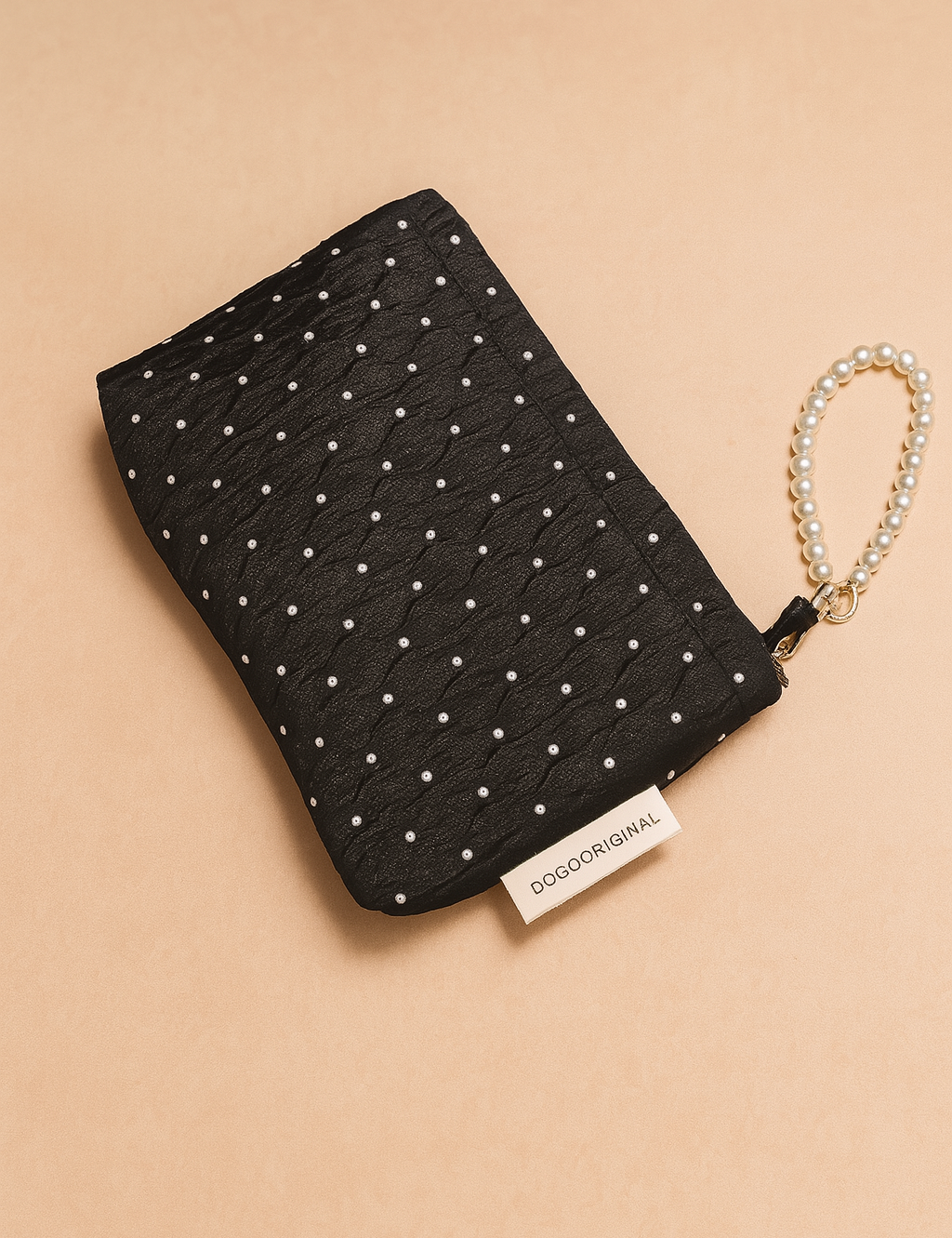 Black quilted clutch with a pearl dot pattern and a pearl-beaded wrist strap, featuring a visible branded fabric tag and elegant textured fabric.