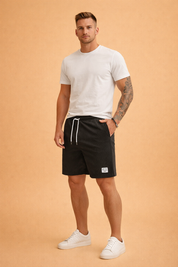 Black ribbed casual shorts made from fine vertical-rib cotton fabric, featuring an elastic waistband with white drawstring, clean side pockets, a straight knee-length cut, and a small woven “POINT” label on the lower hem, paired with a solid sage-green short-sleeve crew-neck T-shirt in smooth jersey fabric and clean white low-top sneakers for a minimal modern casual look.