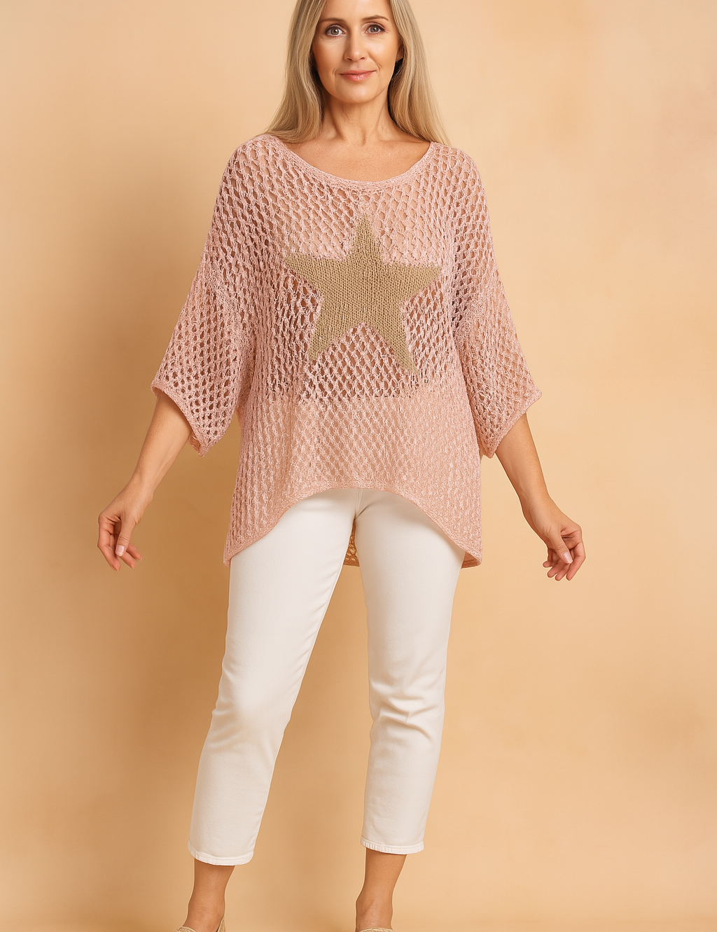 Pastel pink oversized open-knit blouse with a beige star pattern on the front, styled with white cropped pants and beige sandals in a fashion-forward, casual ensemble.