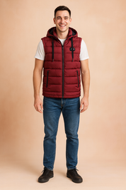 Men’s burgundy quilted puffer vest with hood, zip closure, and two zippered pockets, paired with casual jeans and sneakers for a modern, sporty look