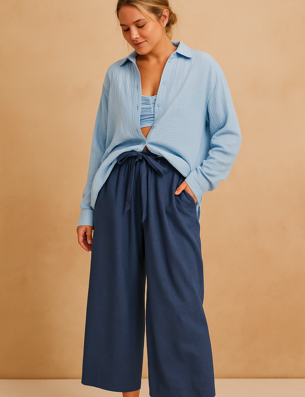 Light blue crinkled button-up shirt paired with a ruched bandeau top and high-waisted navy wide-leg trousers with a matching tie belt.