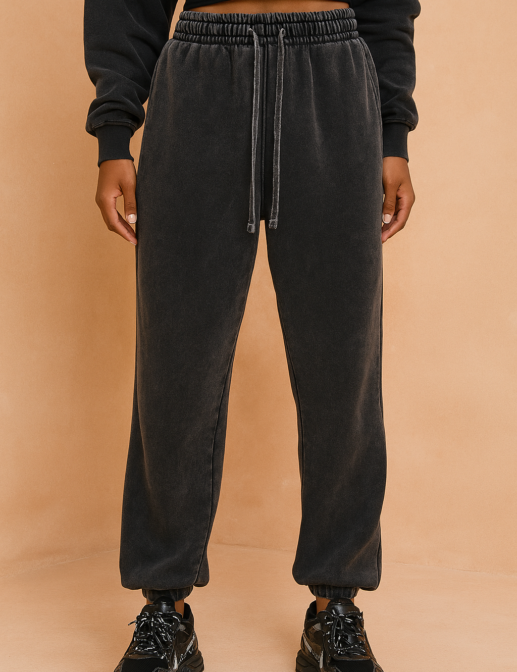 Washed charcoal black sweatpants with a relaxed straight-leg fit, elastic cuffs, long tonal drawstrings, and subtle vintage fade detailing, paired with chunky black sneakers.