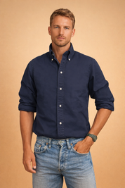 Classic long-sleeve button-down shirt with a clean structured fit, worn tucked into straight-leg denim jeans for a refined casual men’s outfit.