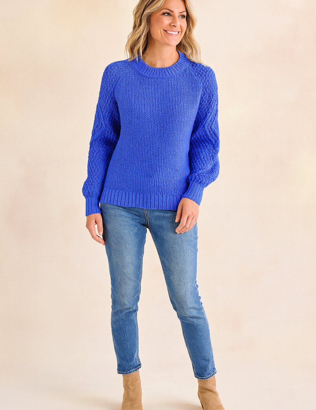 Cobalt blue knit sweater with textured sleeves and ribbed cuffs, paired with light blue jeans and tan suede ankle boots.