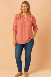 Soft coral V-neck blouse with silver zipper and roll-tab sleeves, styled with medium-blue slim jeans and neutral flats for a fresh, casual look.