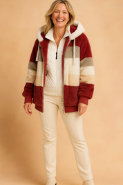 Color-blocked faux fur hooded jacket in rich burgundy, cream, beige, and gray stripes, paired with a white quilted zip-up sweater and slim cream trousers.