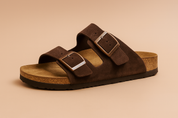  suede slip-on sandal featuring a contoured cork footbed and two wide straps with oversized brown buckles for adjustable comfort.