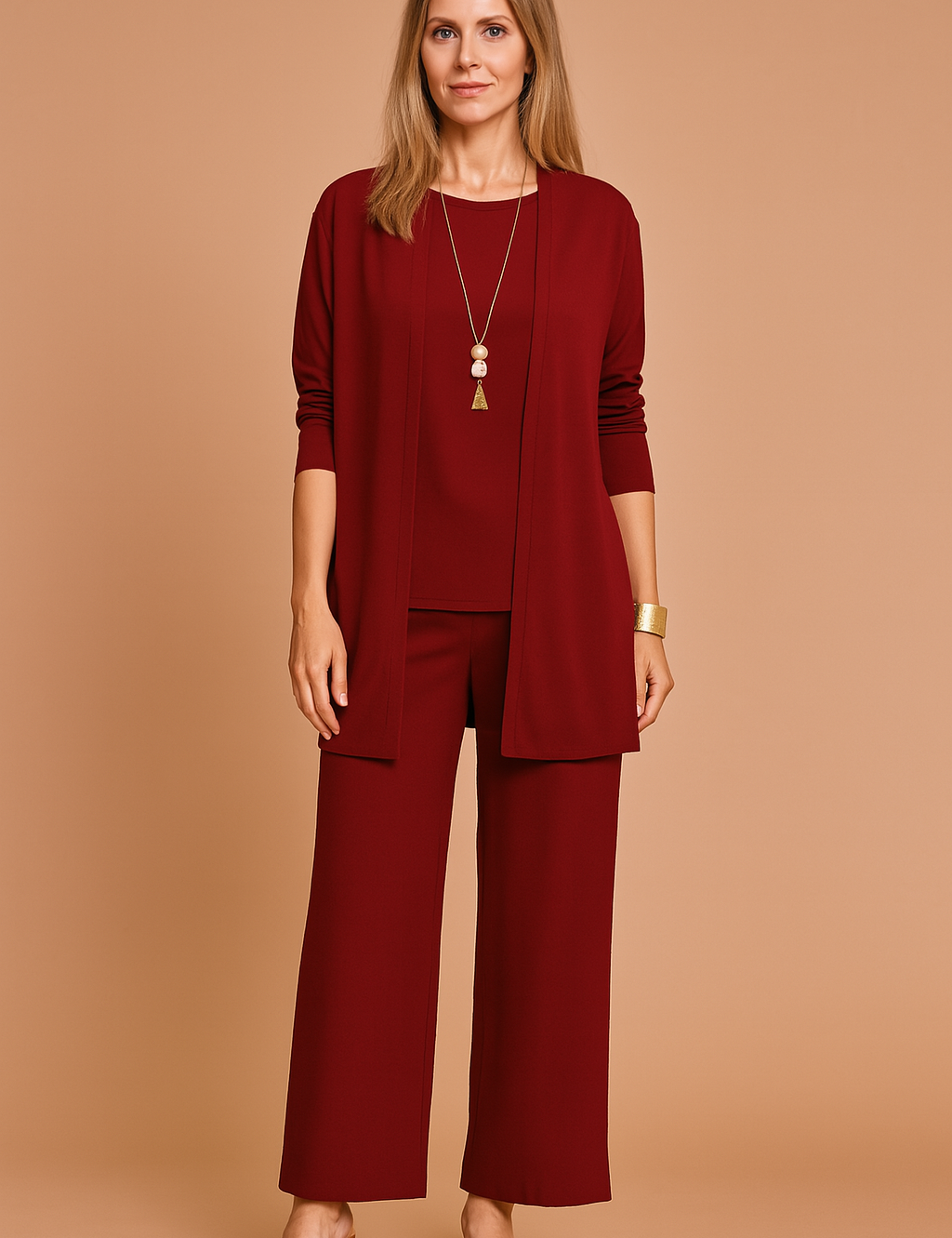 Three-piece dark burgundy women's outfit featuring a long-sleeve open-front cardigan, sleeveless matching blouse, and wide-leg ankle-length trousers in smooth solid fabric, styled with brown block-heel sandals and gold jewelry.