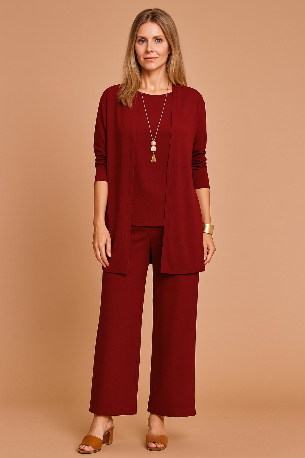 Three-piece dark burgundy women's outfit featuring a long-sleeve open-front cardigan, sleeveless matching blouse, and wide-leg ankle-length trousers in smooth solid fabric, styled with brown block-heel sandals and gold jewelry.
