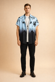 Short-sleeve button-up shirt with a light blue to deep black gradient, featuring a bold black floral print with crisp outlines and consistent color saturation, styled open over a clean white crew-neck T-shirt and finished with a minimal black cord pendant necklace.