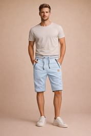 Light blue cotton summer shorts with adjustable drawstring waist, grey ribbed waistband, contrast striped pocket detailing, clean tailored cut, and smooth breathable fabric, styled with a neutral beige short-sleeve t-shirt and minimal white low-top sneakers for a modern casual look