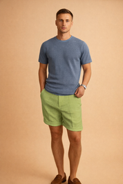 Light green linen shorts with a visible natural linen weave texture, mid-thigh length and clean tailored cut, paired with a solid navy blue short-sleeve crew-neck T-shirt featuring a smooth knit fabric and matte finish, styled with low-profile white athletic sneakers for a clean casual look.