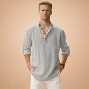 Light grey linen long-sleeve Henley shirt with a relaxed fit, breathable textured fabric, buttoned placket neckline, and roll-tab sleeves, paired with clean white straight-leg trousers for a refined casual look.