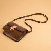 Luxury brown leather handbag with structured silhouette, smooth flap design, precise stitching, and polished gold-tone rectangular clasp