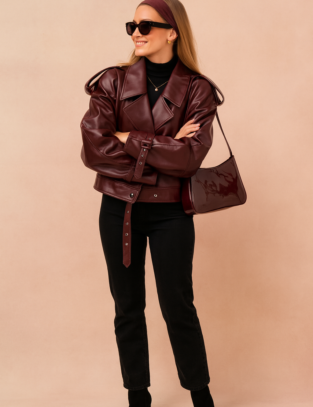 Oversized maroon leather jacket with wide lapel collar, belted cuffs, and waist strap, paired with black high-waisted jeans and heeled ankle boots.