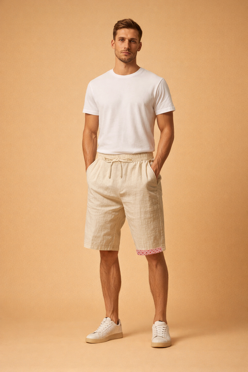 Men’s beige summer drawstring shorts with relaxed fit, textured fabric finish, side pockets, and subtle red geometric hem detail, styled with a clean white short-sleeve t-shirt and minimalist white low-top sneakers for a refined casual warm-weather look