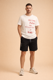 Men’s black athletic shorts with elastic waistband and drawstring, smooth matte fabric, relaxed knee-length cut, subtle Gorilla Power side print in white, paired with a white short-sleeve T-shirt featuring red graphic typography and Asian character print, clean casual summer streetwear outfit