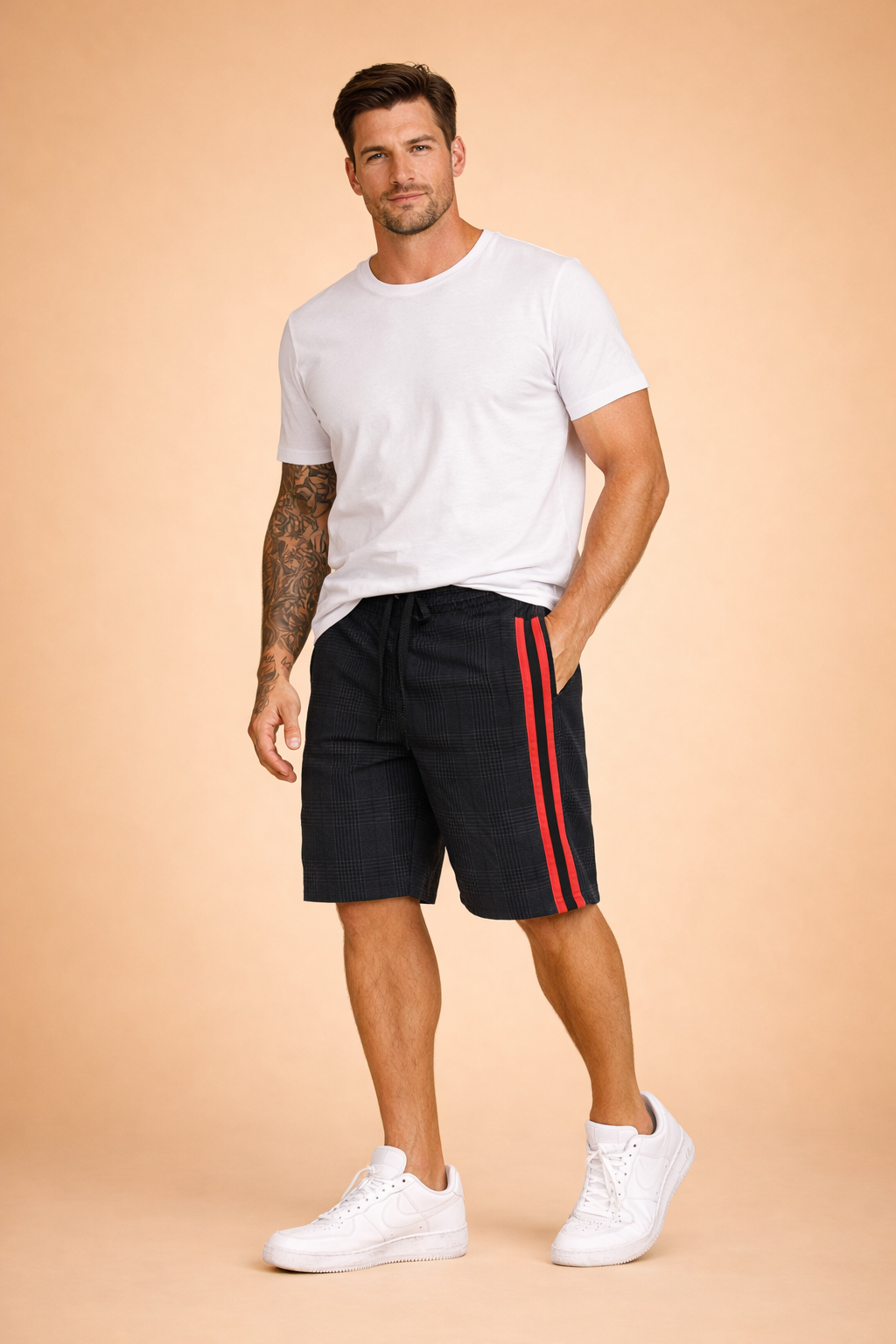 Men’s casual outfit featuring knee-length black and dark grey plaid shorts with a fine check pattern, elastic waistband with black drawstring, and a bold vertical red side stripe, paired with a solid maroon short-sleeve crew-neck T-shirt in smooth cotton fabric and classic white low-top sneakers.