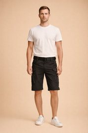 Black tactical cargo shorts with multi-pocket utility design, reinforced stitching, zippered thigh pockets, adjustable waist belt, paired with a clean white fitted short-sleeve T-shirt and minimalist white low-top sneakers for a modern functional menswear look
