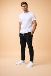 Slim-fit black tapered trousers with elastic waistband and adjustable drawstring, featuring clean side pockets, a smooth structured drape, ankle-length cut, and a modern tailored silhouette paired with low-profile white sneakers.
