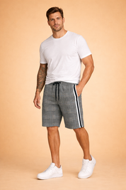 Men’s casual outfit featuring tailored knee-length shorts in a grey plaid check pattern with fine black and white lines, accented by a bold vertical white and black side stripe, elastic waistband with black drawstring, smooth woven fabric texture, paired with a solid light grey short-sleeve cotton T-shirt and clean white low-top sneakers.