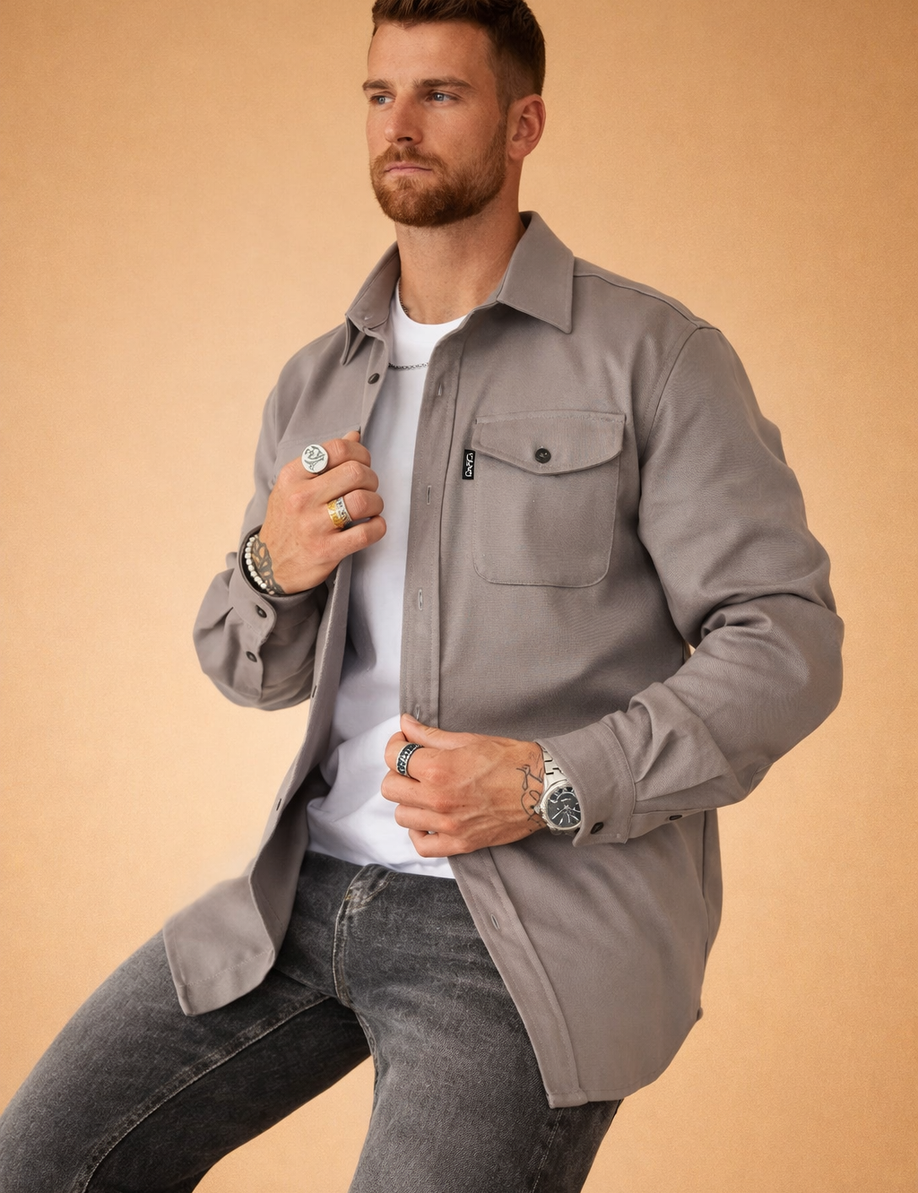 Modern men’s long-sleeve overshirt layered over a fitted crew-neck top, featuring a structured collar, button-front closure, single chest flap pocket, straight hem, and paired with slim straight-leg jeans for a clean, contemporary look.