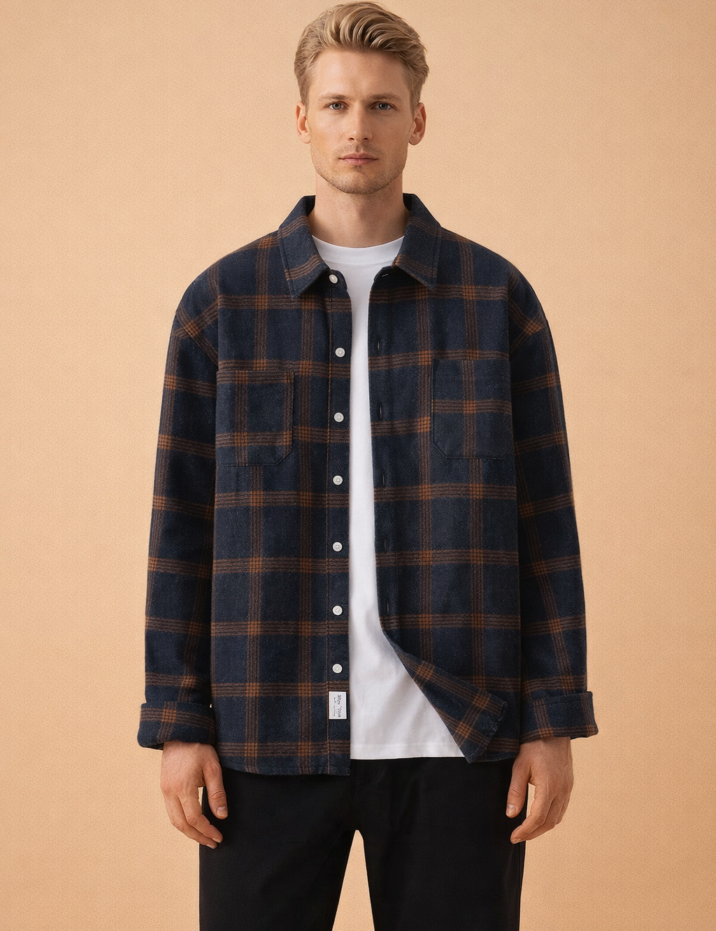 Men’s navy blue plaid overshirt with brown check pattern, long sleeves, button-front closure, chest pockets, styled open over a plain white crew-neck T-shirt and tailored black trousers