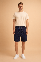 Navy blue men’s casual summer shorts with subtle all over micro dot pattern and small tonal graphic motifs, elastic waistband with drawstring, mid length relaxed fit, lightweight breathable fabric, zippered side pockets, smooth matte finish, tailored casual silhouette