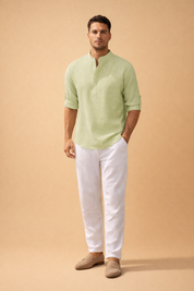 Light sage green textured long-sleeve henley shirt with a fine vertical rib weave, band collar, partial button placket, and roll-tab sleeves, paired with crisp white straight-leg linen trousers and neutral beige suede loafers for a refined casual menswear look.