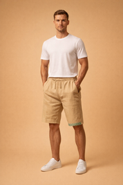 Men’s relaxed-fit sand beige linen shorts with elastic drawstring waist, clean straight hem, subtle natural fabric texture, paired with a minimalist white short-sleeve crew neck T-shirt and clean low-profile white lace-up sneakers for a modern summer casual look