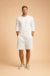 Light summer outfit featuring a relaxed long-sleeve white shirt paired with tailored light sand shorts showcasing a fine vertical textured stripe pattern, finished with a clean elastic waistband and drawstring, styled with minimal neutral footwear for a refined warm-weather look.