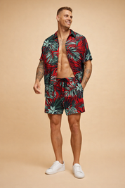 Men’s tropical summer set featuring a short-sleeve button-up shirt and matching drawstring shorts with a bold red base and detailed green and teal palm leaf print, lightweight fabric with a relaxed tailored cut designed for warm-weather wear.