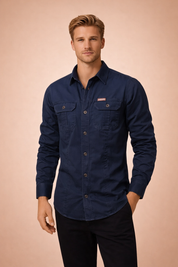 Men’s long-sleeve utility shirt with classic collar, front button closure, dual chest flap pockets, structured seams, tailored fit, and a clean workwear-inspired silhouette.