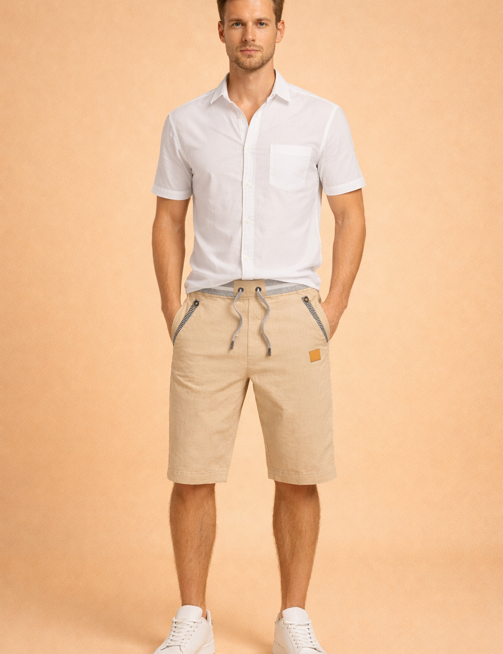 Men’s white short sleeve button-up shirt paired with beige cotton drawstring shorts featuring striped pocket trim, ribbed waistband, and matching beige fabric tone, styled with clean white low-top sneakers for a refined casual summer look.