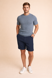 Men’s minimalist outfit featuring a smooth solid white short-sleeve T-shirt paired with tailored navy blue shorts, crafted in a clean matte fabric with a structured yet relaxed fit, finished with light grey athletic sneakers for a modern casual look.