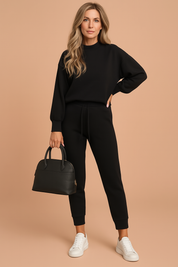 Black long-sleeve crewneck pullover paired with high-waisted black jogger pants featuring a drawstring waist, styled with a structured black handbag and white low-top sneakers.