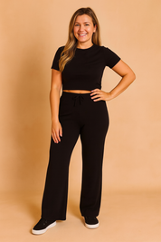 Black short-sleeve crop top paired with high-waisted wide-leg black pants featuring a drawstring waist, crafted from soft stretch knit fabric for all-day comfort.