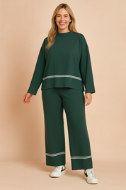 Dark green two-piece loungewear set featuring a long-sleeve top with white piping along the hem and wide-leg pants with matching piping at the ankles and side seams, made from soft, textured knit fabric.