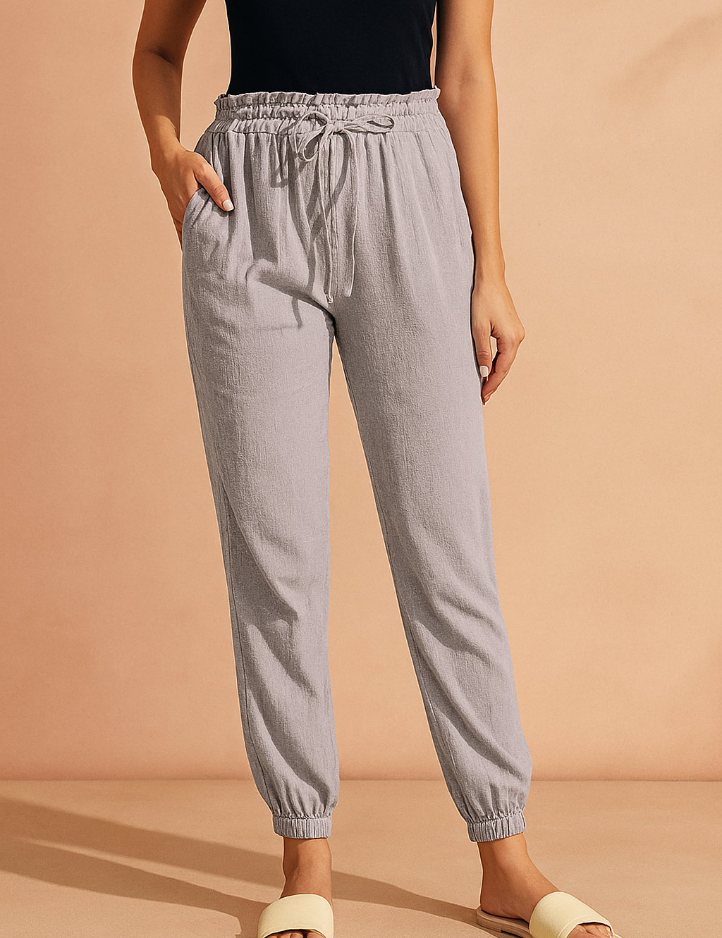 Light gray jogger pants with a textured fabric, drawstring waist, side pockets, and elasticated cuffs, styled with a tucked-in black sleeveless top and beige slide sandals.