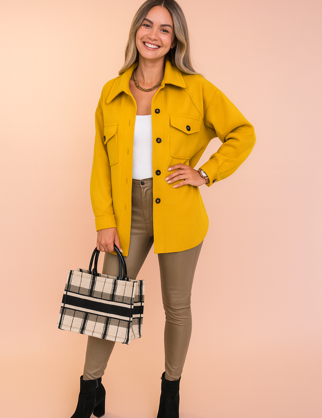 Mustard yellow button-up shirt jacket with front flap pockets, styled with a white tank top, beige fitted leather-look pants, black ankle boots, and a plaid structured handbag.