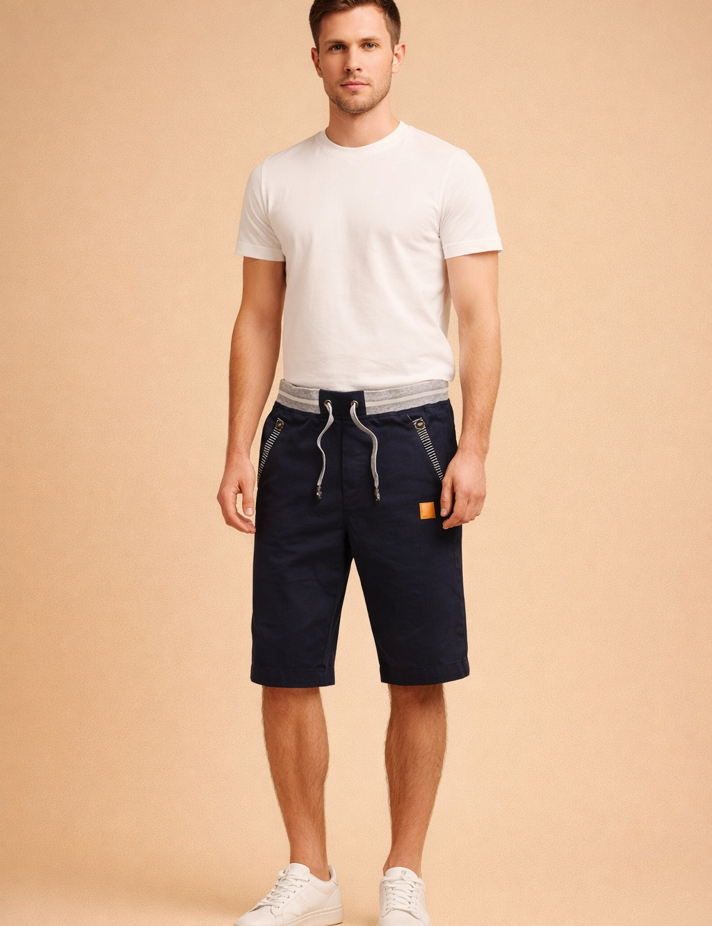 Navy blue men’s knee-length cotton shorts with adjustable drawstring waist, grey ribbed waistband detail, zippered front pockets with striped trim, subtle vertical pinstripe lining at hem, and clean solid fabric finish paired with minimalist white low-top sneakers